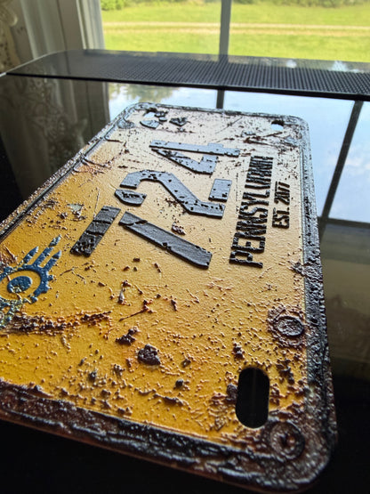 A distressed yellow license plate featuring a rusty black finish, with 'PENNSYLVANIA' and the number '724' embossed on the front.